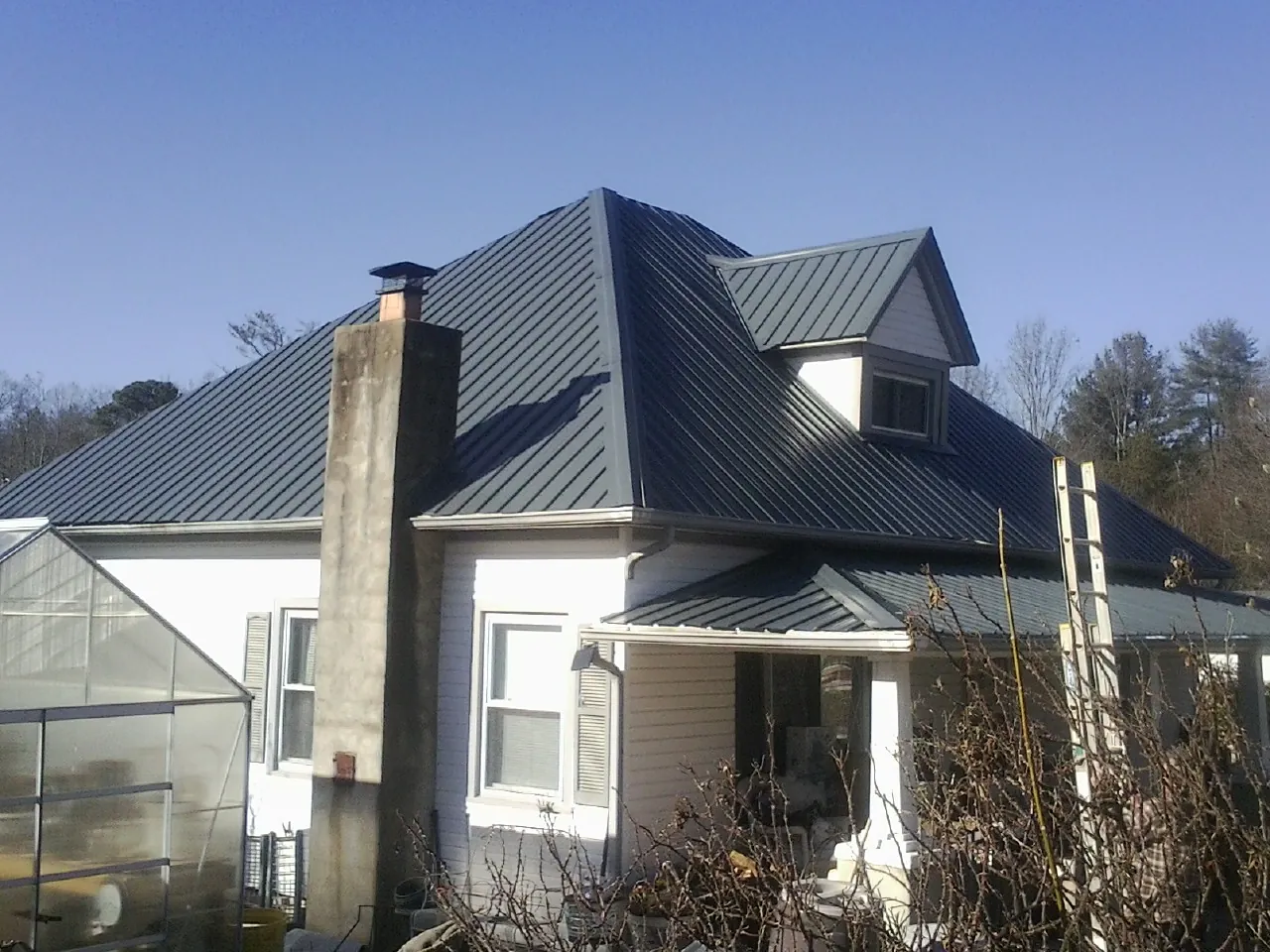 Dark blue standing seam metal roof on a white farmhouse with dormer — Slate & Tile Roof Repair by Roofing Brothers in Stratton