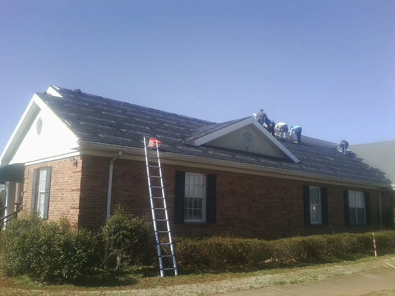 Crew tearing shingles off a brick ranch roof with a ladder set — Emergency Roof Repair work by our crew in Stratton