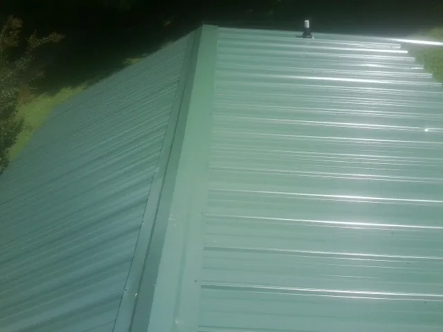 New green metal panels meeting at the ridge of a roof — Flat Roof Repair work by our crew in Stratton