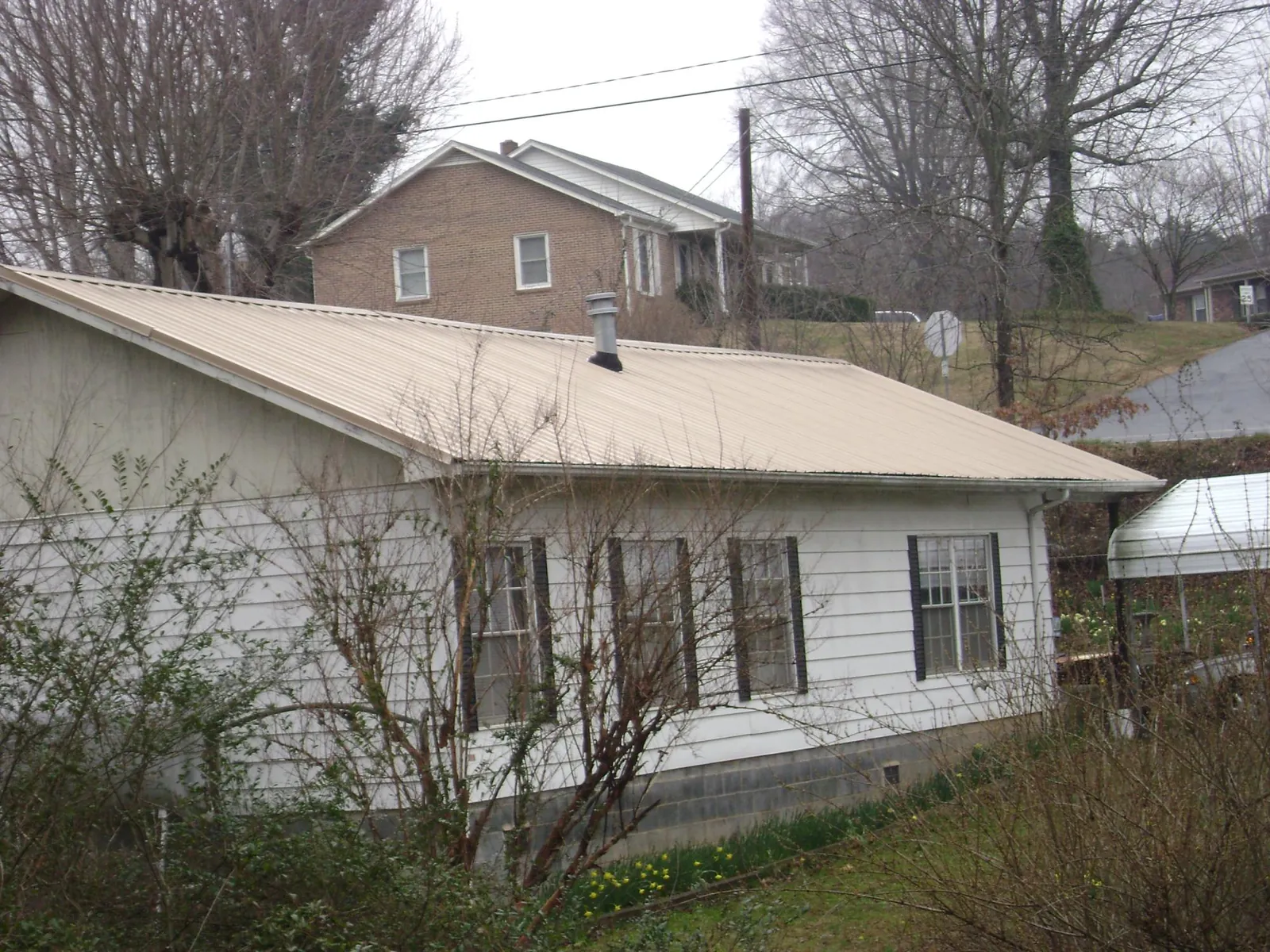 Tan metal roof on a white sided house set into a hillside — Commercial Roofing by Roofing Brothers in Stratton